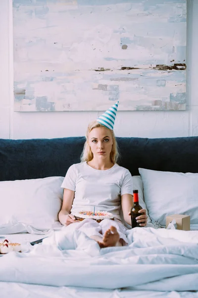 ワインとケーキだけでベッドで誕生日を祝っている間カメラを見て落ち込んでいる女性 — ストック写真