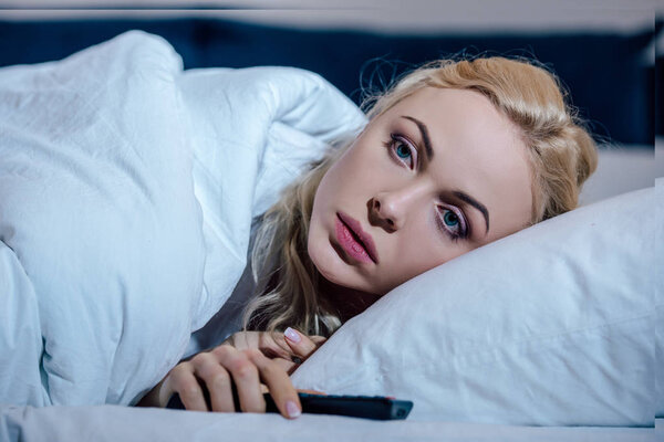 selective focus of beautiful upset woman covered in blanket and lying in bed at home