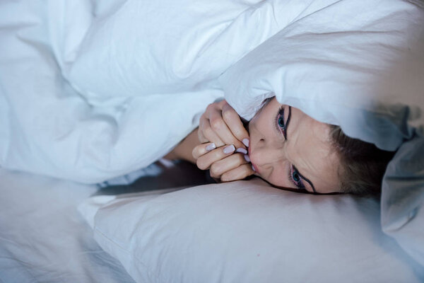 frightened woman covered in blanket biting nails in bed at home