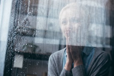 jest evde yağmur damlaları ile pencereden ağlayarak dua ile üzgün yetişkin kadın
