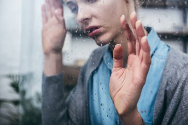 Kırpılan üzgün yetişkin kadın yağmur damlaları ile ev dokunaklı pencere görünümünü