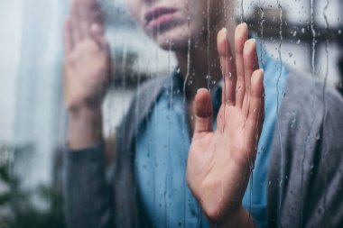 Kırpılan yetişkin kadın yağmur damlaları ile ev dokunaklı pencere görünümünü