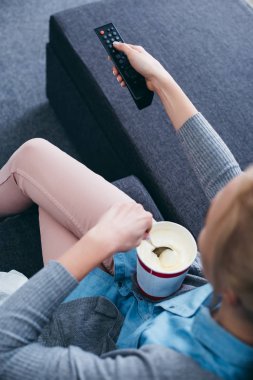 tv izlerken dondurma ve uzaktan kumanda ile kanepede oturan kadın kırpılmış görünümünü