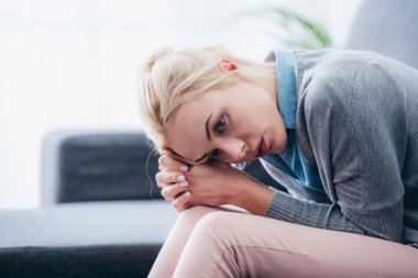 selective focus of upset woman with folded hands sitting at home  clipart