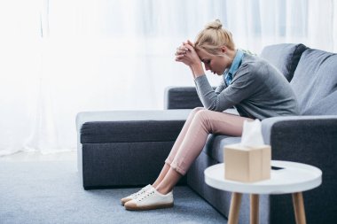 depressed woman with folded hands sitting at home on couch clipart