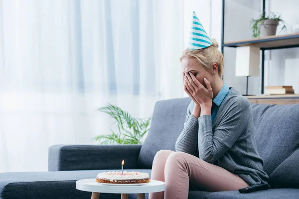 upset woman in party hat crying while celebrating birthday at home alone