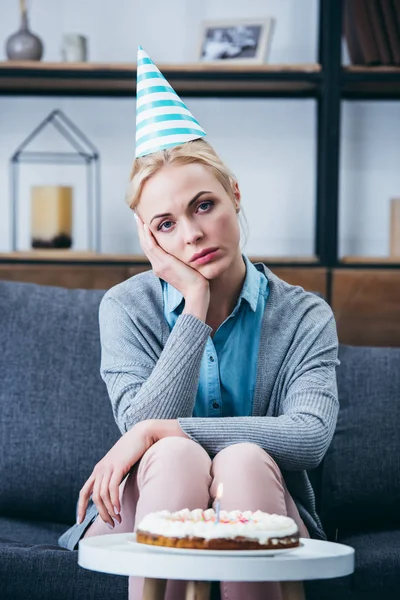 パーティー帽子手で頭を支え 一人で家で誕生日を祝っている間カメラ目線の悲しい女 — ストック写真