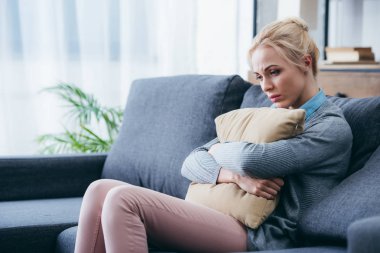 depressed woman sitting on couch and holding pillow at home clipart