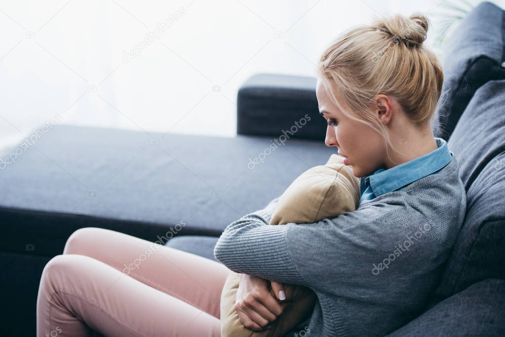 depressed woman sitting on couch and holding pillow at home