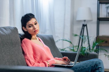 Hintli kadın kanepede dizüstü kullanarak bindi ile