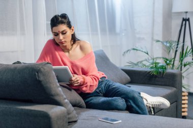 Dijital tablet ve smartphone ile kanepede oturan bindi çekici Hintli kadın