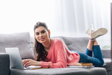 kitap ve kanepe üstünde laptop ile eğitim bindi çekici Hintli kadın
