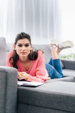 female indian student with bindi studying with notebook on sofa clipart