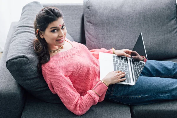 Leende Indisk Kvinna Med Bindi Använder Laptop Liggande Soffan — Stockfoto