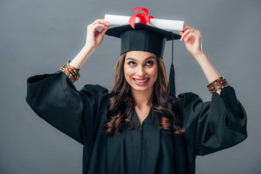 neşeli Hint öğrenci mezuniyet şapkalı diploma, gri izole holding