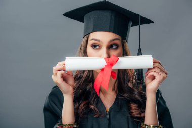 female indian student in graduation hat holding diploma, isolated on grey clipart