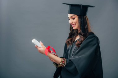 şapkalı diploma, gri izole tutan akademik elbisesi ve mezuniyet mutlu Hint öğrenci