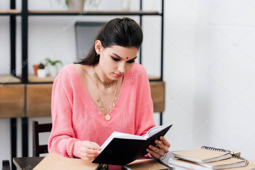 indian student with bindi studying with notebooks and reading book at home