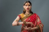 attraktive indische Frau gestikuliert in traditioneller Kleidung, isoliert auf grau 