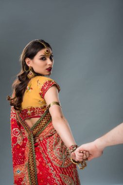 indian couple in traditional clothing holding hands isolated on grey  clipart