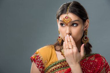 shocked attractive indian woman closing mouth, isolated on grey  clipart