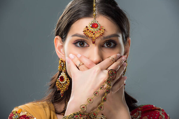 elegant shocked indian girl closing mouth with hands, isolated on grey 