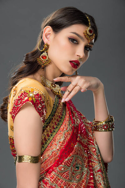 elegant indian woman posing in traditional sari and accessories, isolated on grey 