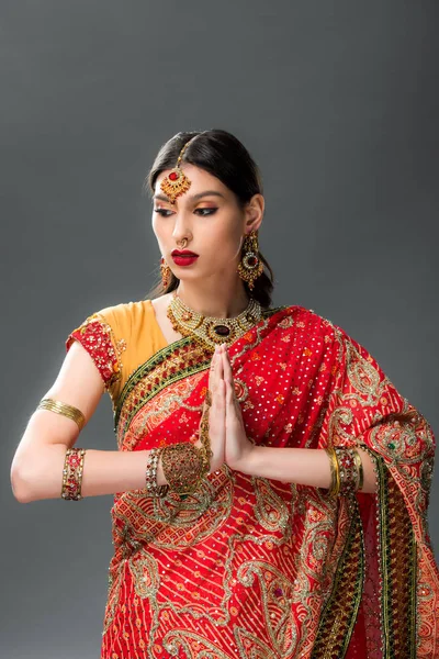 beautiful indian woman in traditional clothing with namaste mudra, isolated on grey