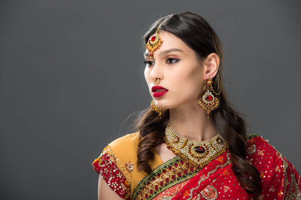 attractive indian woman in sari and bindi on head, isolated on grey 