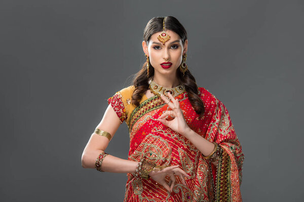 attractive indian woman in sari and accessories with gyan mudra, isolated on grey 