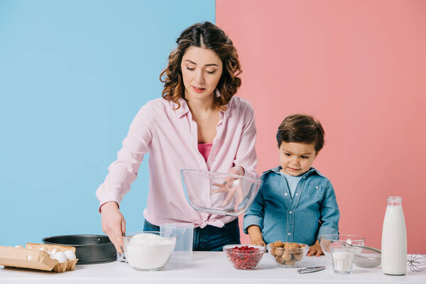 pretty mother and cute son preparing cooking ingredients together on bicolor background