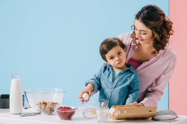 sevimli küçük oğlu yumurta tutarak ve kameraya bicolor arka plan üzerinde seyir yardımcı anne