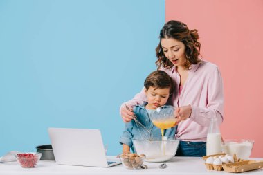 ekleme anne bicolor arka plan üzerinde küçük oğlu ile birlikte pişirme sırasında kaseye yumurta şanti