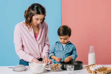 Anne ve sevimli oğlu birlikte bicolor arka plan üzerinde beyaz mutfak masasında yemek 