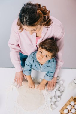 bir anne ile küçük oğlu hamuru mutfak masasında ışık arka plan üzerinde birlikte yayıyoruz üstten görünüm