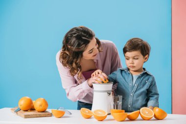 sevimli küçük çocuk anne juicer bicolor arka plan üzerinde üzerinde taze portakal suyu sıkma içinde yardım