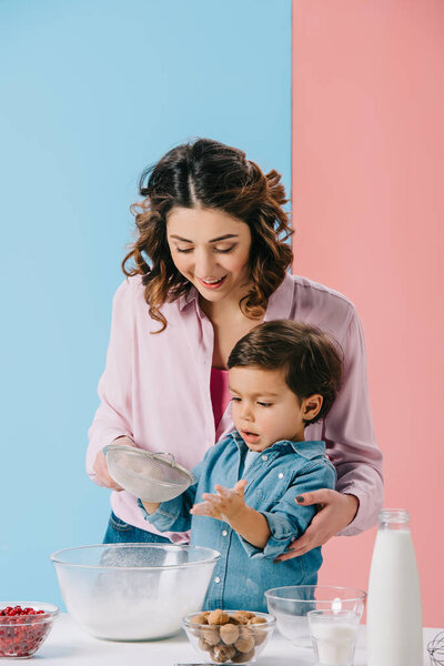 beautiful mother with cute little son cooking together on bicolor background