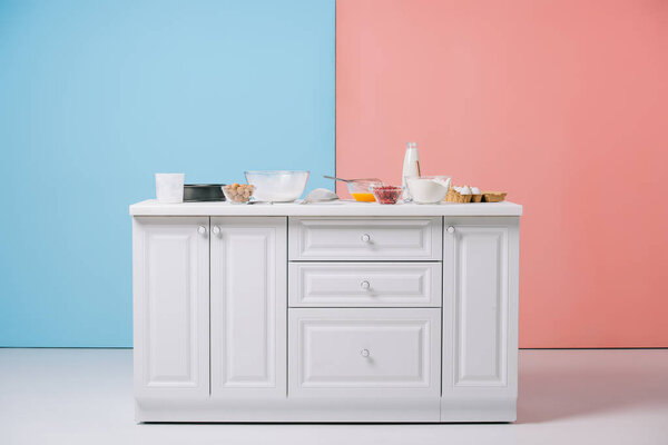 белый кухонный стол с различными кухонными принадлежностями и продуктами на двухцветном фоне
