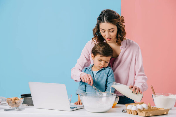 cute little boy looking at laptop display while mother cracking walnut on bicolor background