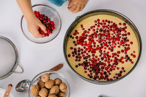 сверху вид ребенка добавления клюквы в тесто в форме выпечки на белом фоне
