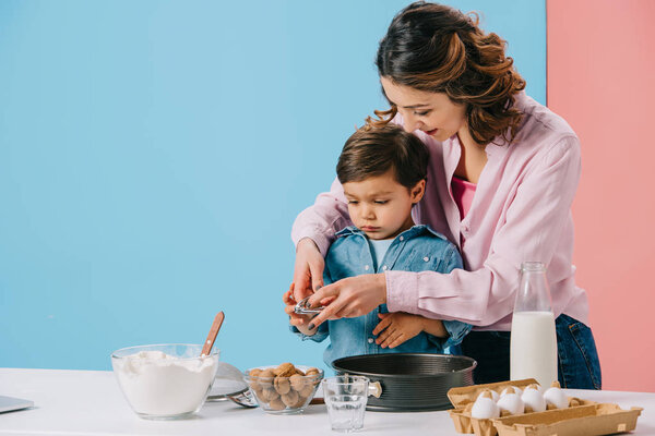 pretty mother with cute little son cracking walnuts while cooking together on bicolor background 