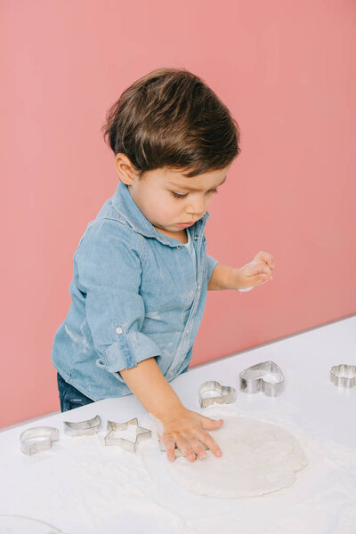 little boy cuts figures in dough with dough molds isolated on pink