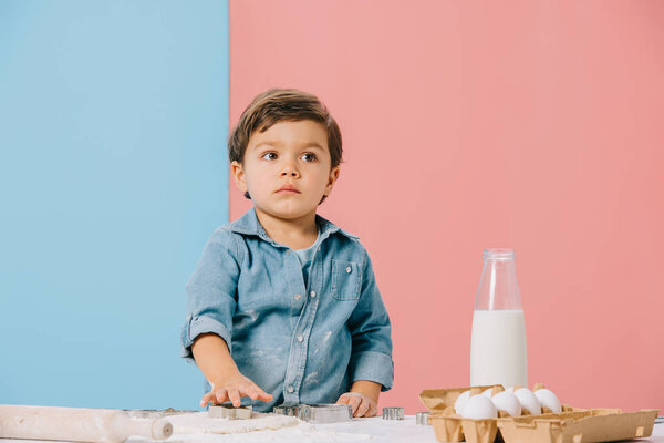 little kid cutting figures in dough at white kitchen table on bicolor background 