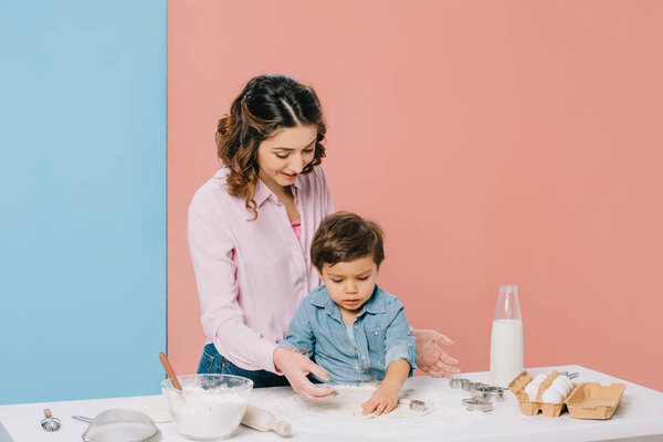 smiling mother with cute little son cooking pastry together on bicolor background 