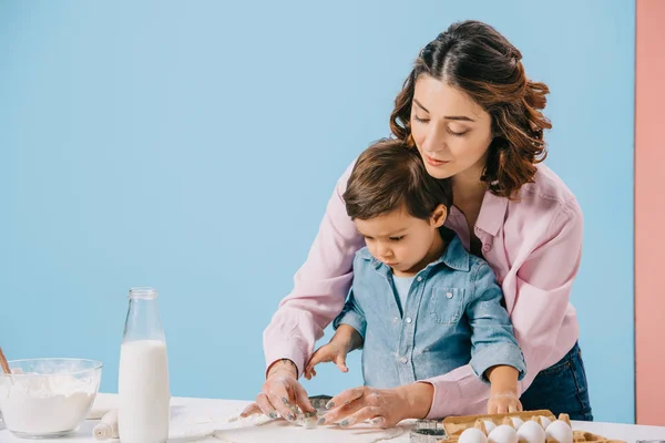 母とかわいい息子二色の背景に白いキッチン テーブルで一緒に菓子を調理 — ストック写真