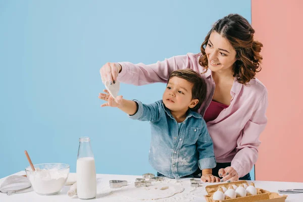 二色の背景に一緒にお菓子を作っている間母の手でクッキーに手を伸ばすかわいい男の子 — ストック写真