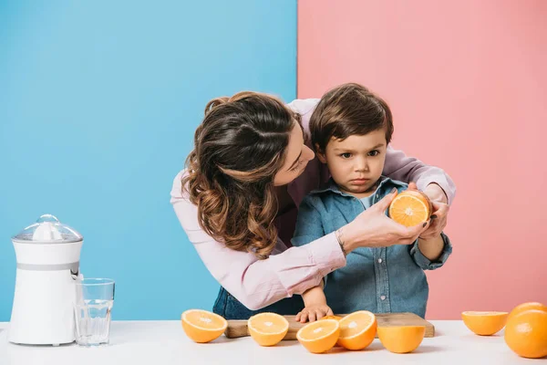 Mama Luând Jumătate Portocaliu Mâna Fiului Mic Serios Fundal Bicolor — Fotografie, imagine de stoc