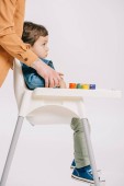 mother hugging little son sitting on highchair with watercolors set on table isolated on white