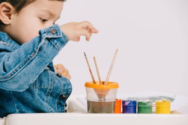 sevimli küçük çocuk boyama fırça üzerinde beyaz izole masada suluboya boya ile sandalyesi üzerinde otururken seçme
