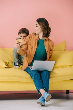 gülümseyen anne gösteren kredi kartı laptop kullanırken küçük oğlu için